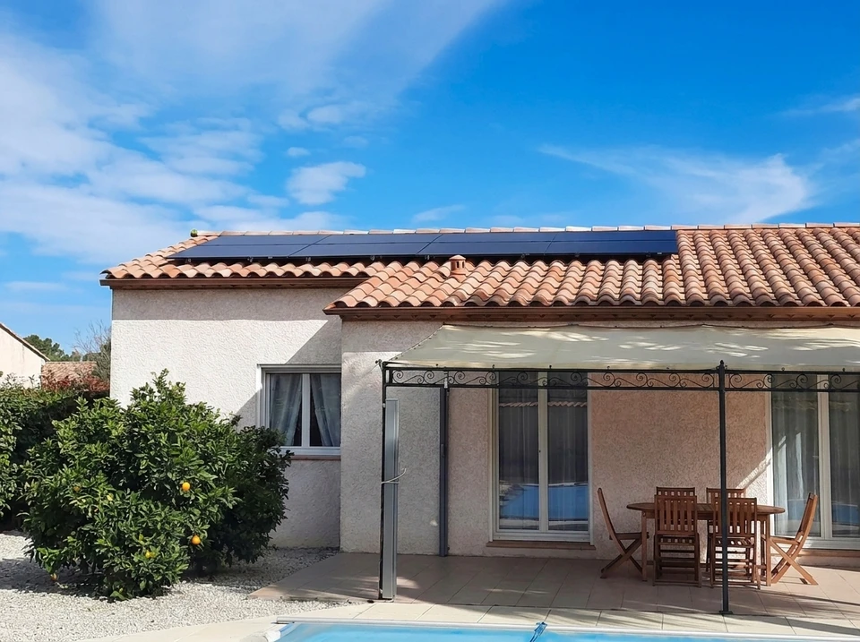 Unité extérieure de climatisation split-system Panasonic, posée sur supports métalliques réglables au sol, installée contre un mur en stuc beige, bordé d'une muret en briques rouges et d'une grille en fer forgé